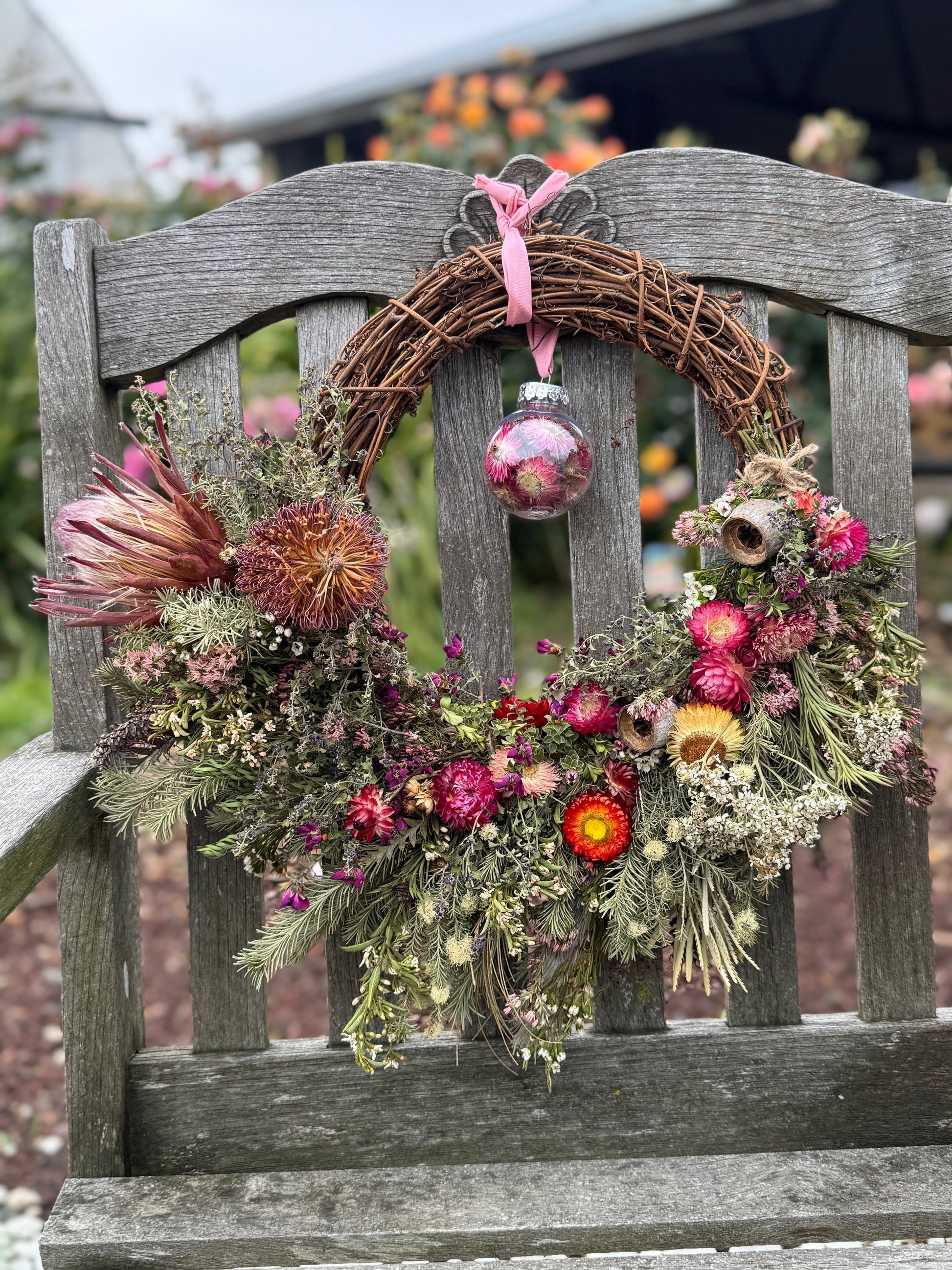 Decorative wreath with flowers and a pink ornament on a wooden bench.